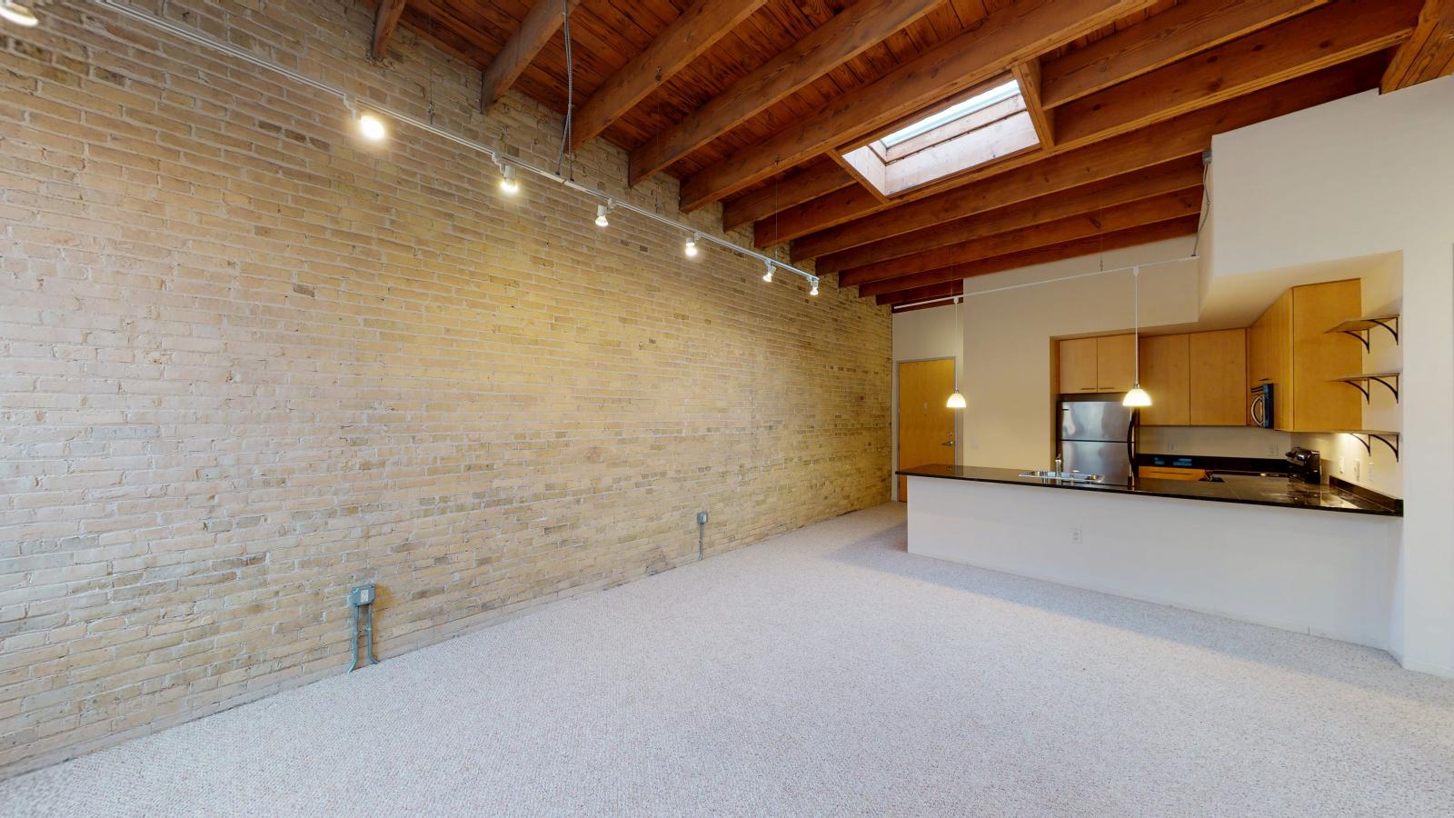 One bedroom apartment with a modern kitchen featuring granite countertops, and exposed brick, at Tobacco Lofts at The Yards in downtown Madison